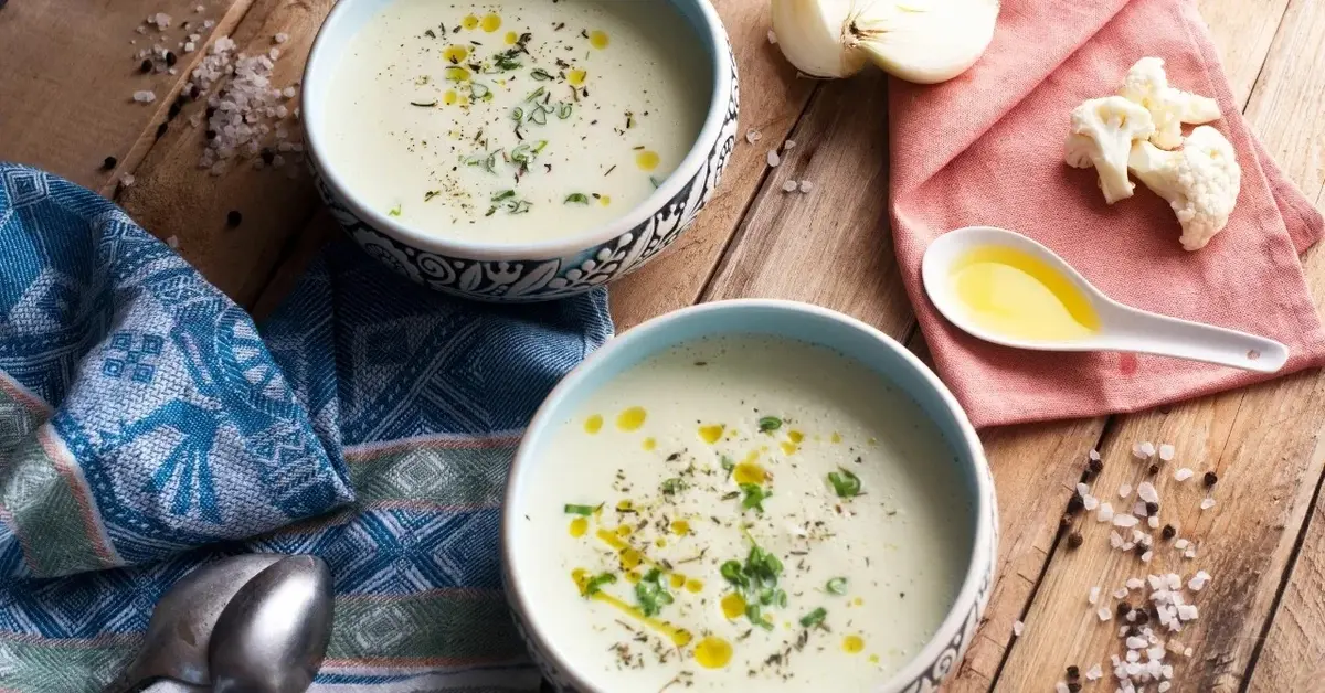 Zupa krem cebulowa w dwóch miseczkach na blacie drewnianym z ozdobnymi ściereczkami