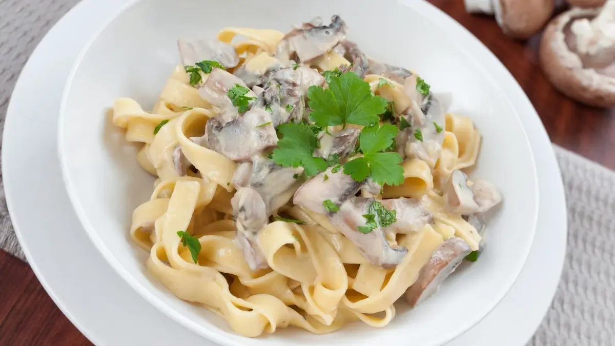 Makaron tagliatelle z sosem pieczarkowym na białym talerzu
