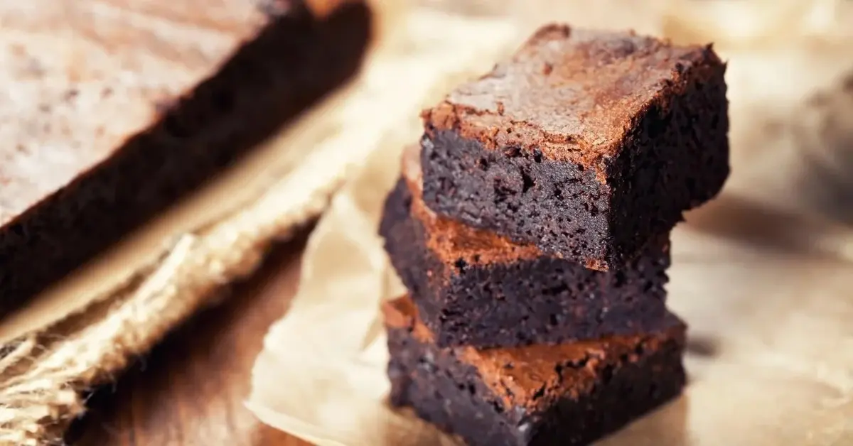 Trzy kawałki ciasta brownie ułożone na sobie na papierze do pieczenia