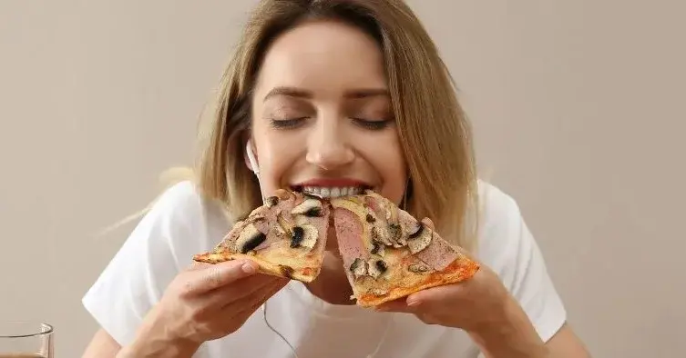 Kobieta je pizzę i na stole ma jeszcze inne dania
