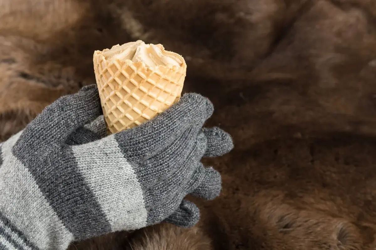 Osoba w zimowych rękawiczkach, trzyma loda w rożku