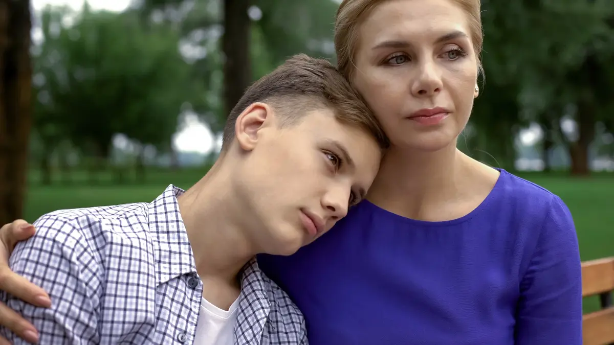 matka siedzi z synem w parku , sy n opiera głowę na jej ramieniu