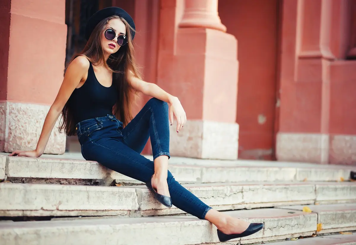 young beautiful brunette girl in a hat, sunglasses, t-shirt and jeans, walking on the ancient city