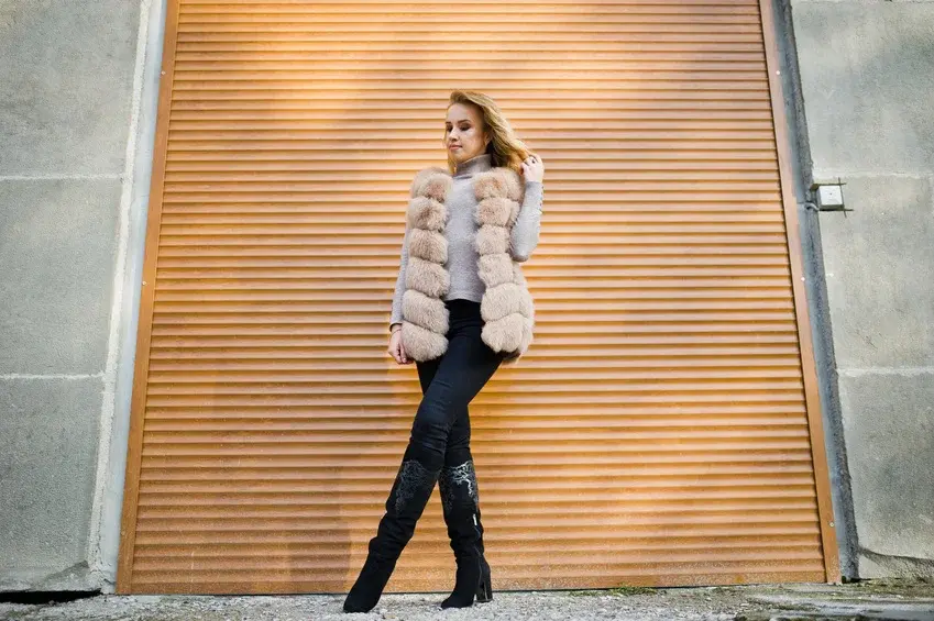 Blonde girl at fur coat against wall with shutters.