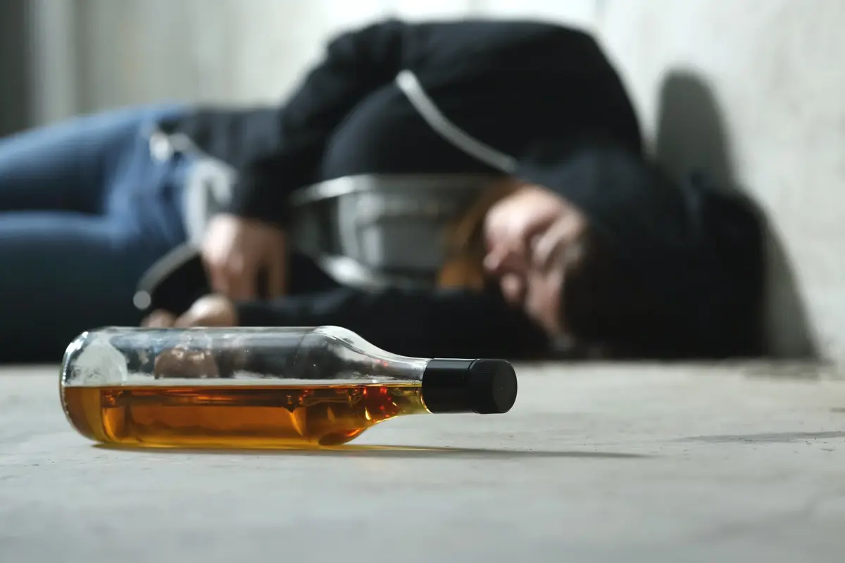 pijany nastolatek leży na podłodze, butelka na pierwszym planie