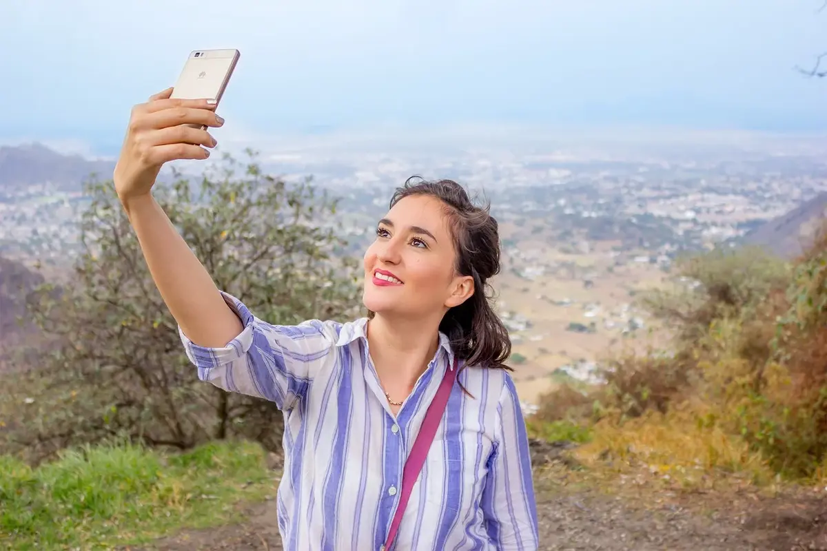 kobieta robi sobie selfie smartfonem na tle wzgórz
