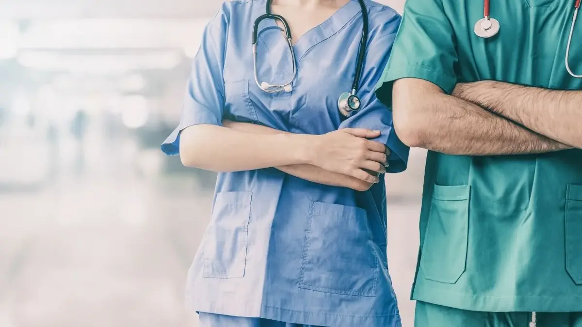 dwie osoby w strojach lekarzy stoją z założonymi rękoma na szpitalnym korytarzu