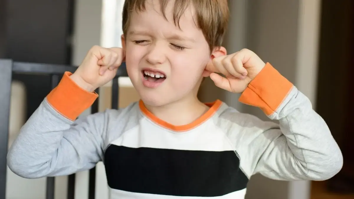 chłopiec z grymasem na twarzy wkłada palce do uszu
