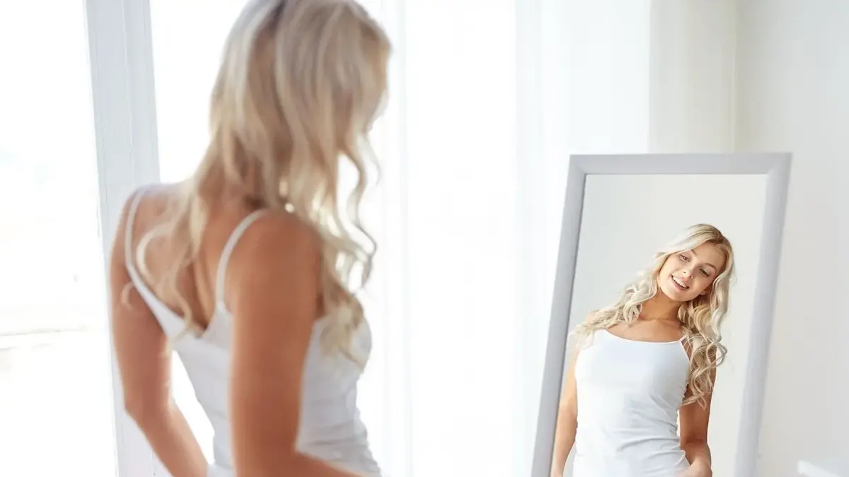 blondynka w białej bluzce stoi przed lustrem