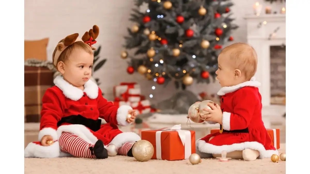 Dwoje rocznych dzieci w stroju mikołajów. W tle prezenty, bombki i choinka.