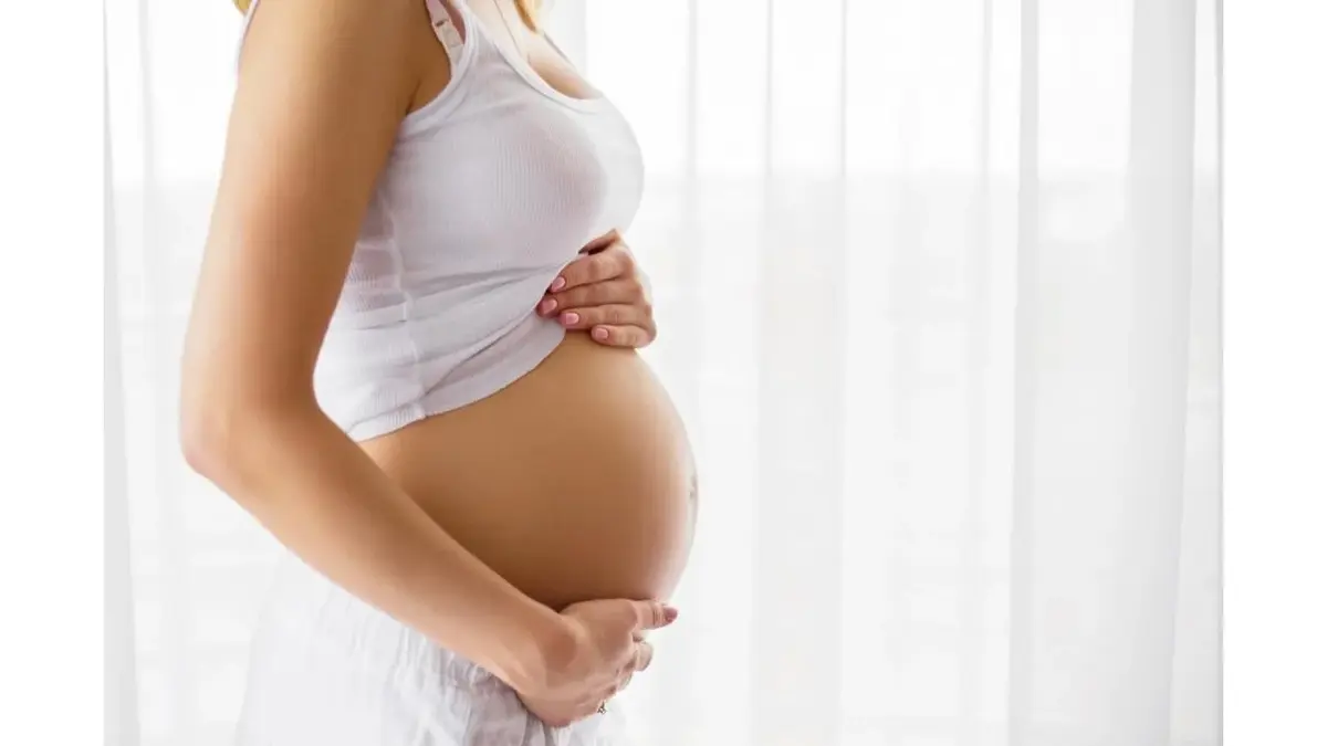 Widać brzuch kobiety w ciąży, kobieta go obejmuje.