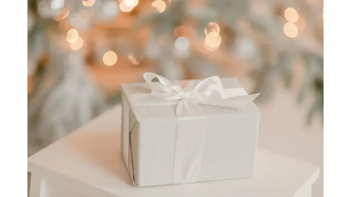 Prezent w białym opakowaniu, na tle świątecznych lampek