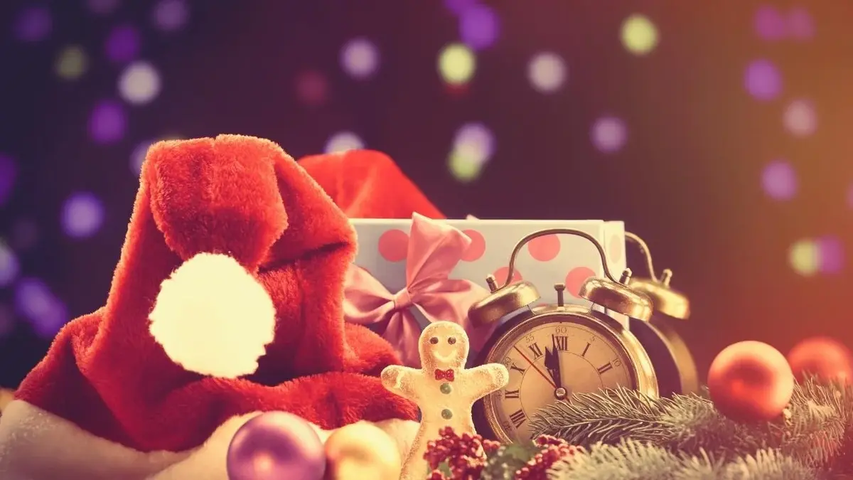 Prezent, czapka mikołaja, bombka, gałąź choinki , zegarek i piernikowy ludzik.