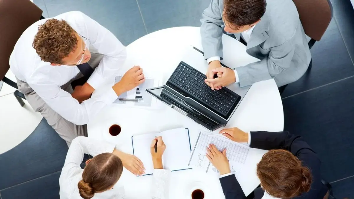 4 osoby w strojach biznesowych siedzą dookoła stołu, widok z góry