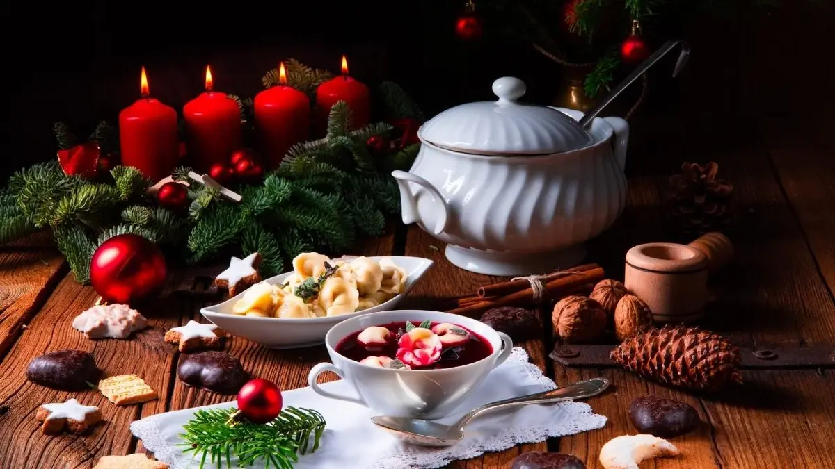 Wigilijny barszcz z uszkami, orzechy, pierniki i ciastka w kształcie gwiazdek. Obok świece.