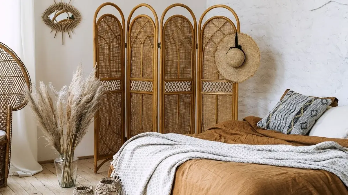 Łóżko z brązową narzutą i białym kocem, obok wiklinowego parawanu