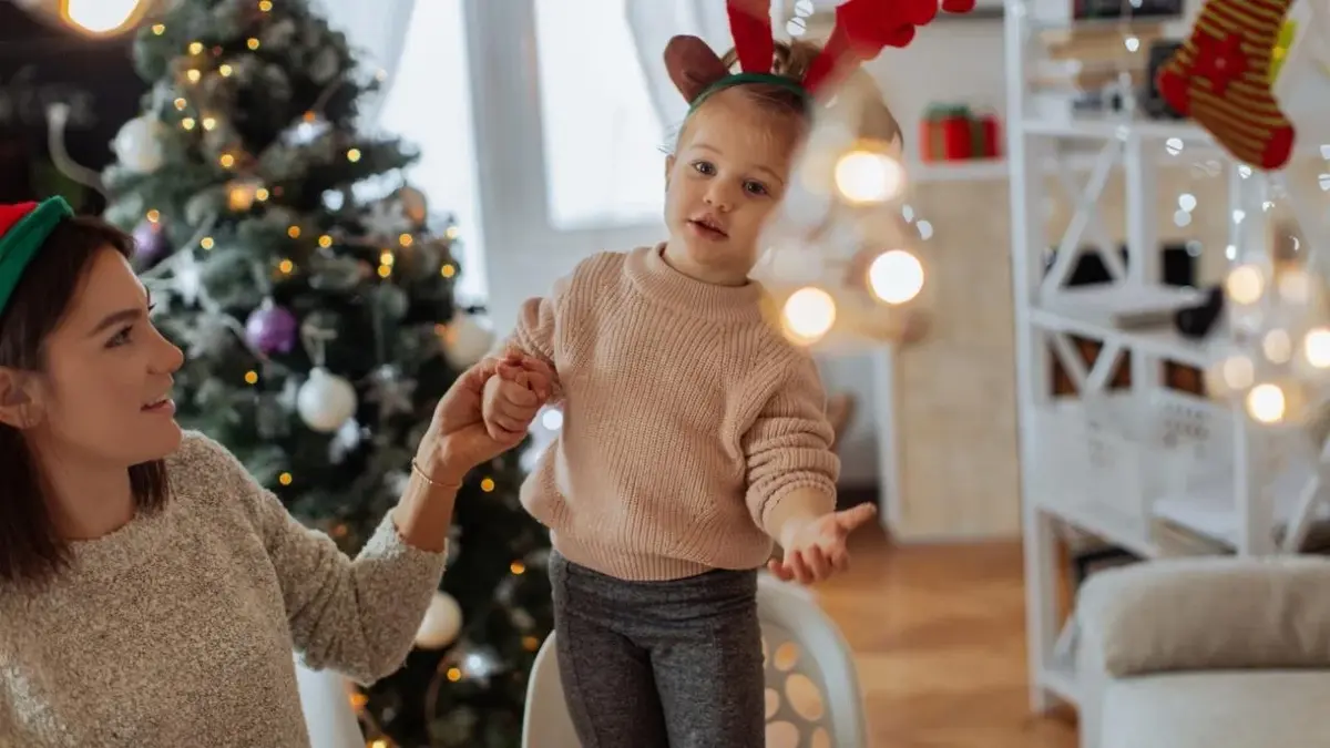 Dziewczynka śpiewa kolędy z mamą. W tle choinka i lampki.