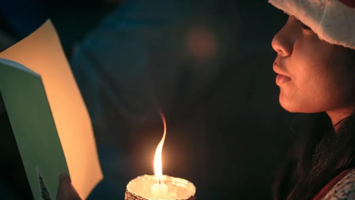 Dziewczynka trzyma zapaloną świecę i śpiewa kolędy.