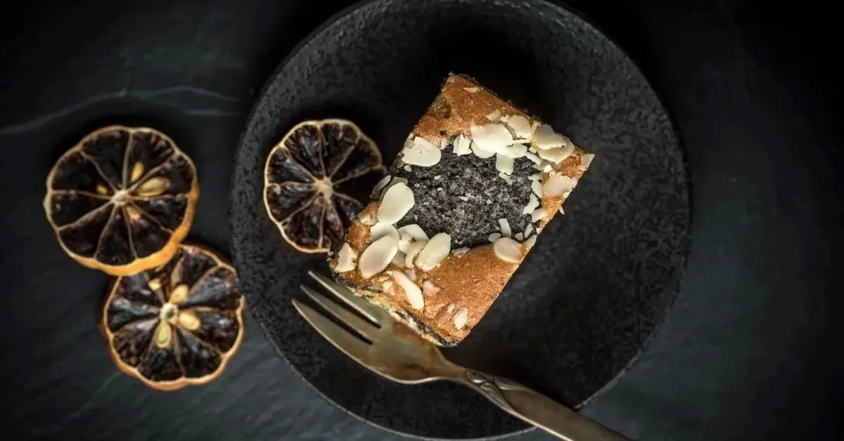 Kawałek makowca na czarnym talerzu udekorowanym suszonymi plastrami pomarańczy