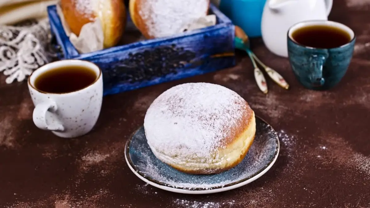 Pączki z pudrem, obok stoją dwie herbaty.