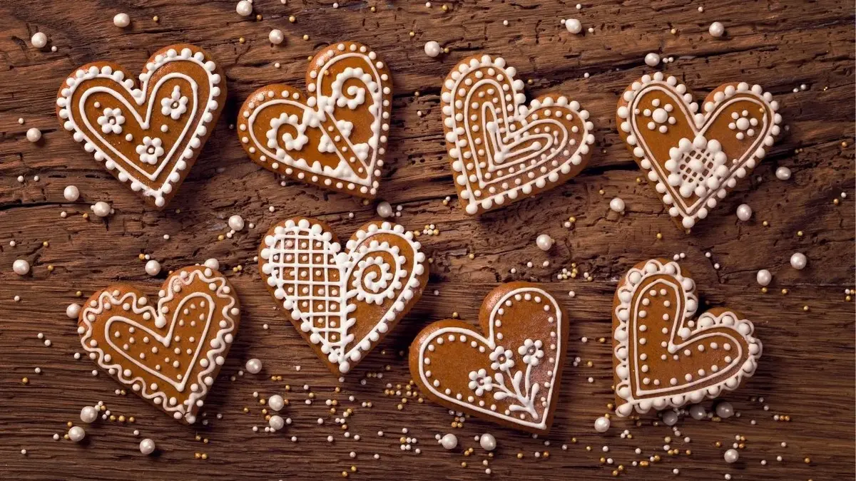 Polukrowane pierniki-serduszka leżące w dwóch rzędach na drewnianym stole