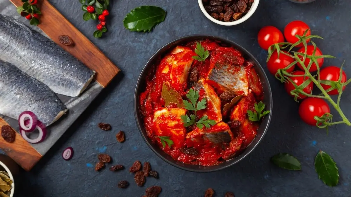 Śledzie w pomidorowym sosie w miseczce obok ryby i pomidorków koktajlowych