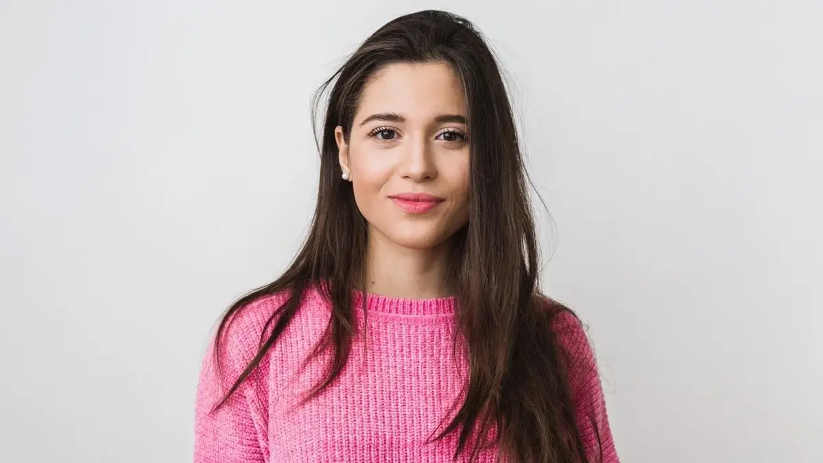 Kobieta o długich, brązowych włosach w różowym swetrze