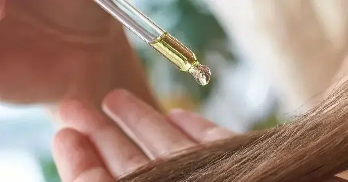 Dłonie kobiety wylewającej kroplę oleju z nerkowców na włosy