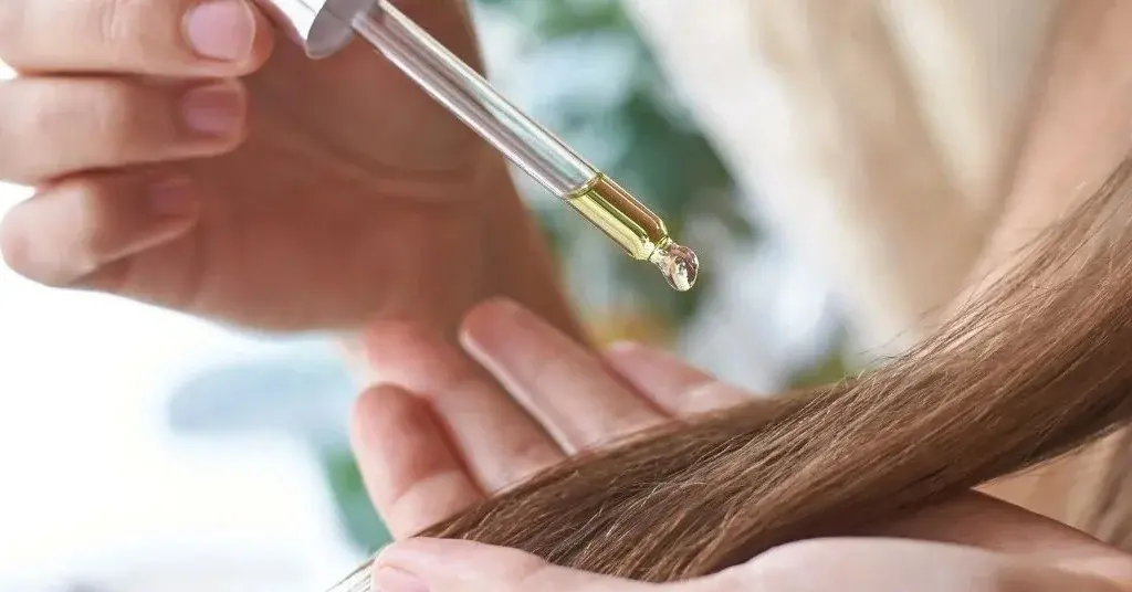 Dłonie kobiety wylewającej kroplę oleju z nerkowców na włosy