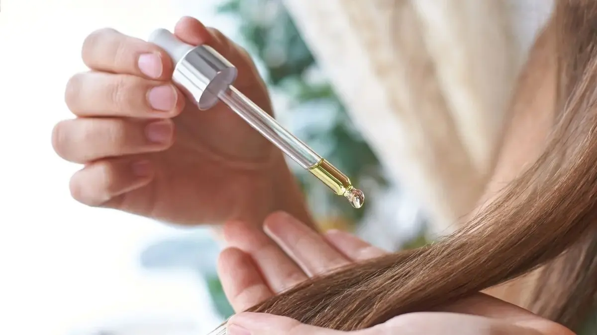 Dłonie kobiety wylewającej kroplę oleju z nerkowców na włosy
