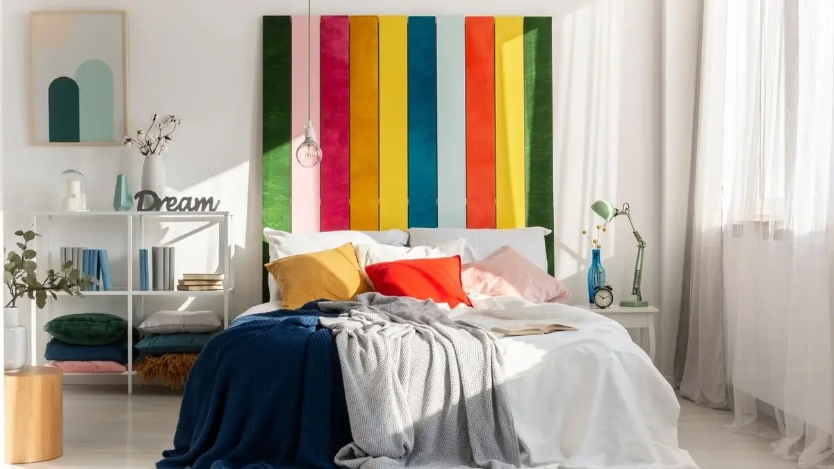 Zagłówek z kolorowego drewna na ścianie w białej sypialni nad łóżkiem z kolorowymi poduszkami