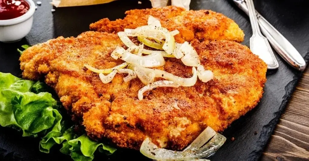 Kotlet schabowy z frytkami, surówką i sosami.