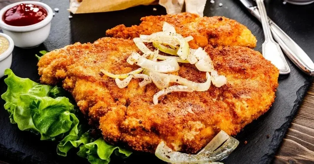 Kotlet schabowy z frytkami, surówką i sosami.