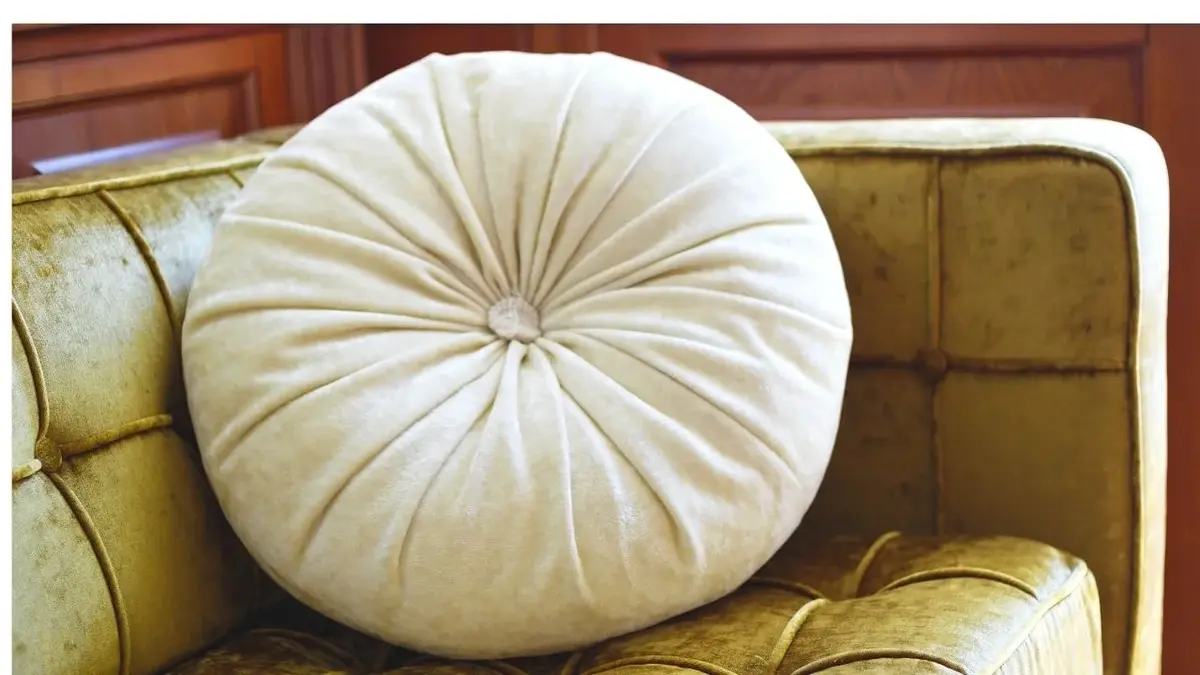 Okrągła poduszka z weluru w kremowym kolorze na welurowej sofie