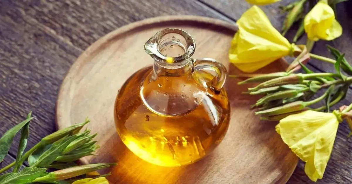 Olej z wiesiołka w dzbanku. Obok leżą kwiaty wiesiołka.