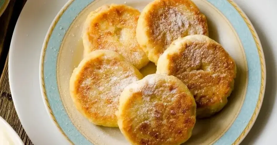 Placuszki bananowe posypane cukrem pudrem, obok śmietana i płynna czekolada.