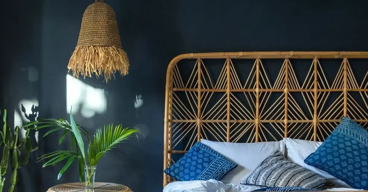 Plecione wezgłowie z rattanu na tle granatowej ściany obok boho lampy wiszącej