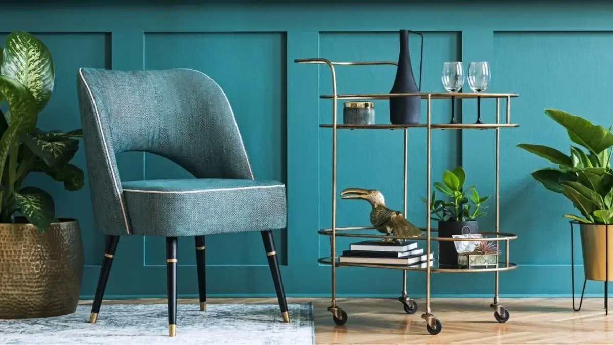 Złoty barek na kółkach z kieliszkami i bibelotami w błękitnym salonie obok błękitnego krzesła