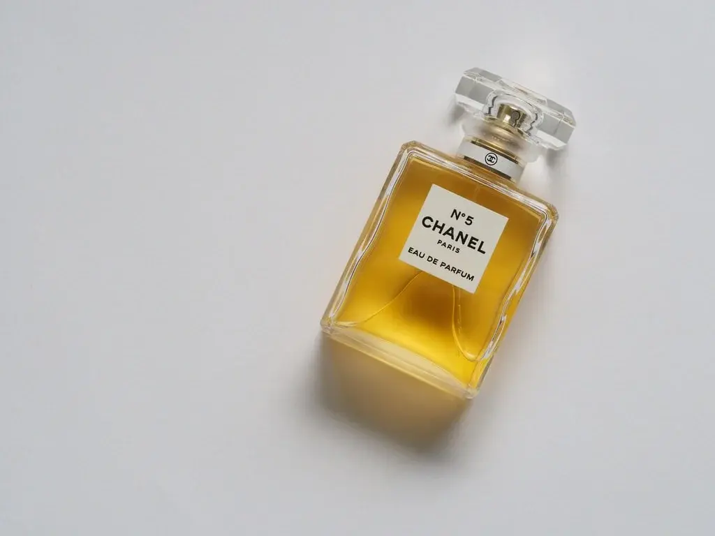 Flakonik damskich perfum o bursztynowym kolorze na białym tle