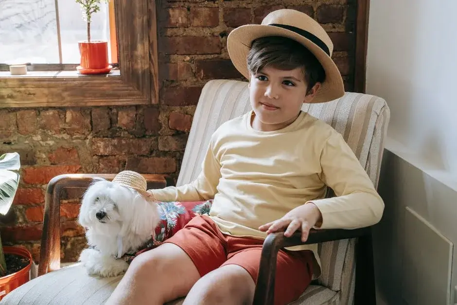 Chłopiec w słomkowym kapeluszu siedzi na fotelu z białym psem