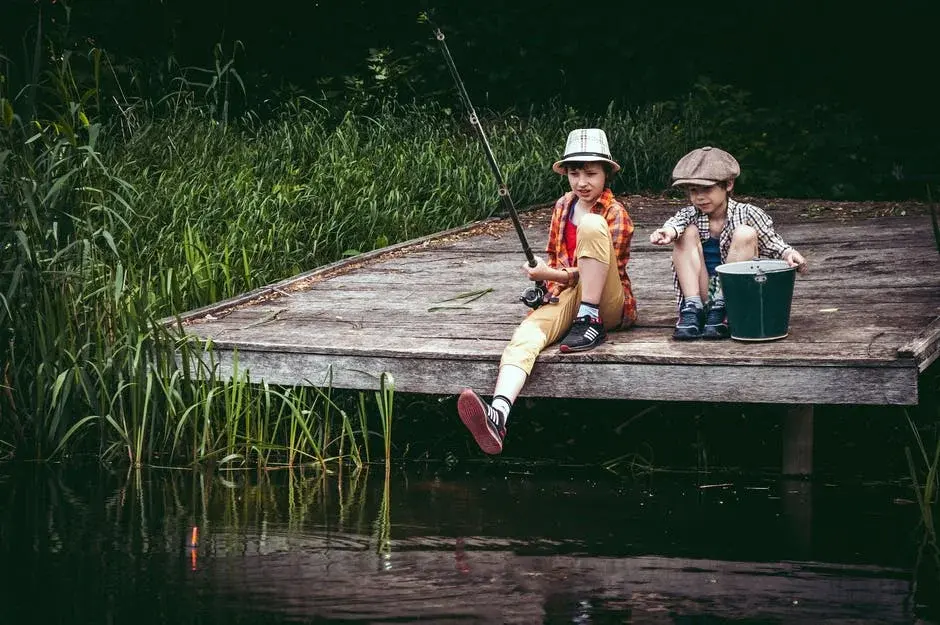 Chłopcy siedzą na drewnianym pomoście i łowią ryby na wędkę