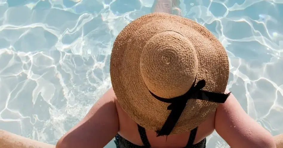 Szykowna kobieta w kapeluszu leży w basenie