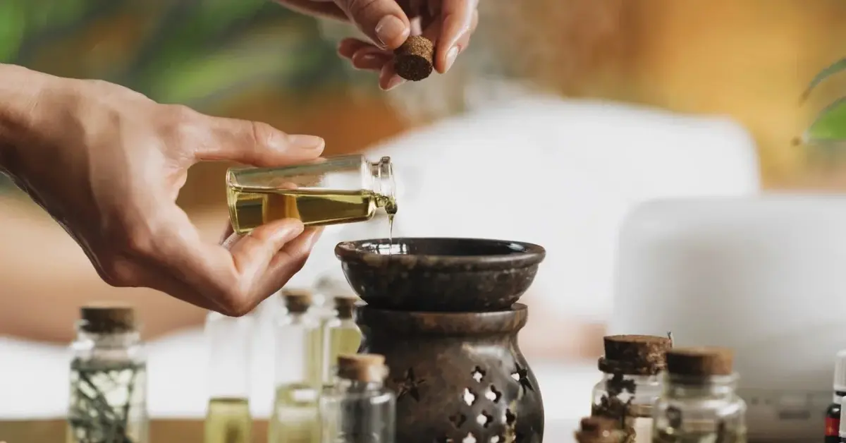 Zastawiony olejkami w buteleczkach i próbówkach stół, ludzkie dłonie mieszają olejki w specjalnym kociołku