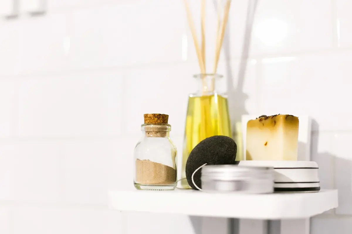 W białej łazience na półce obok wazonu z patyczkami zapachowymi stoją słoiki i puszeczki z olejkami