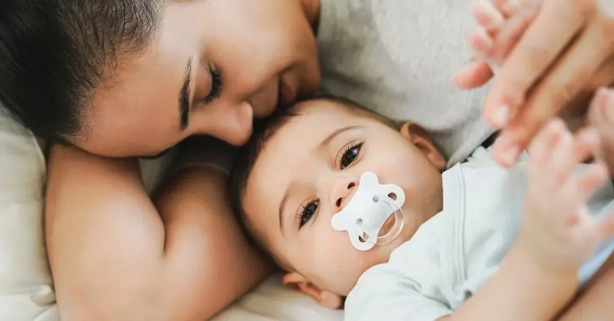 Matka z niemowlakiem ze smoczkiem tuli się w łóżku w domu zaopatrzonym w produkty dla niemowląt