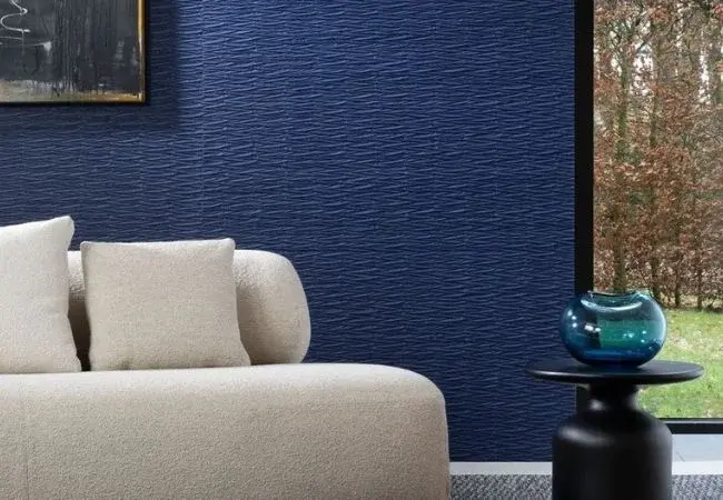 Ściana z dekoracyjną kobaltową tapetą ścienną, przed nią białą sofa z poduchami o stolik z wazonem