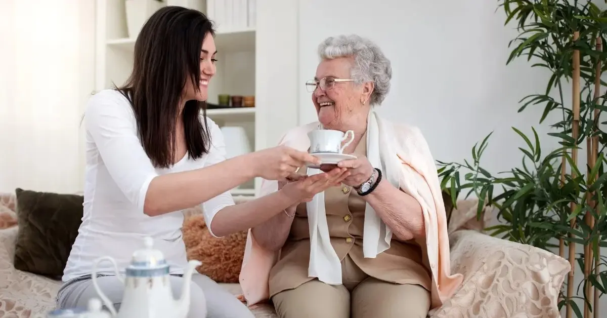 babcia z wnuczką siedzą na kanapie i piją herbatkę