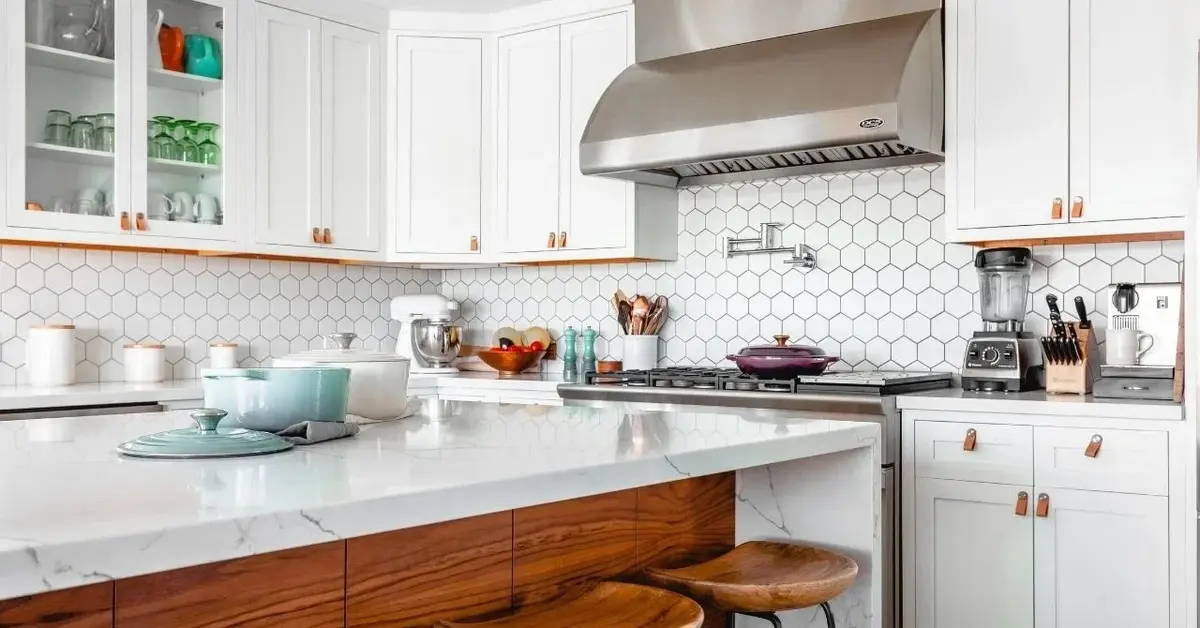 Backsplash z białych płytek ceramicznych heksagonalnych w białej kuchni z drewnianą wyspą kuchenną i metalowym okapem
