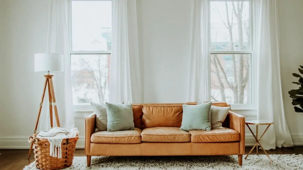 Brązowa kanapa na tle okna z białymi zasłonami