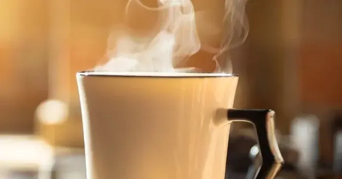 Biały kubek z czarnym uchem. Nad naczyniem unosi się para z gorącej kawy.